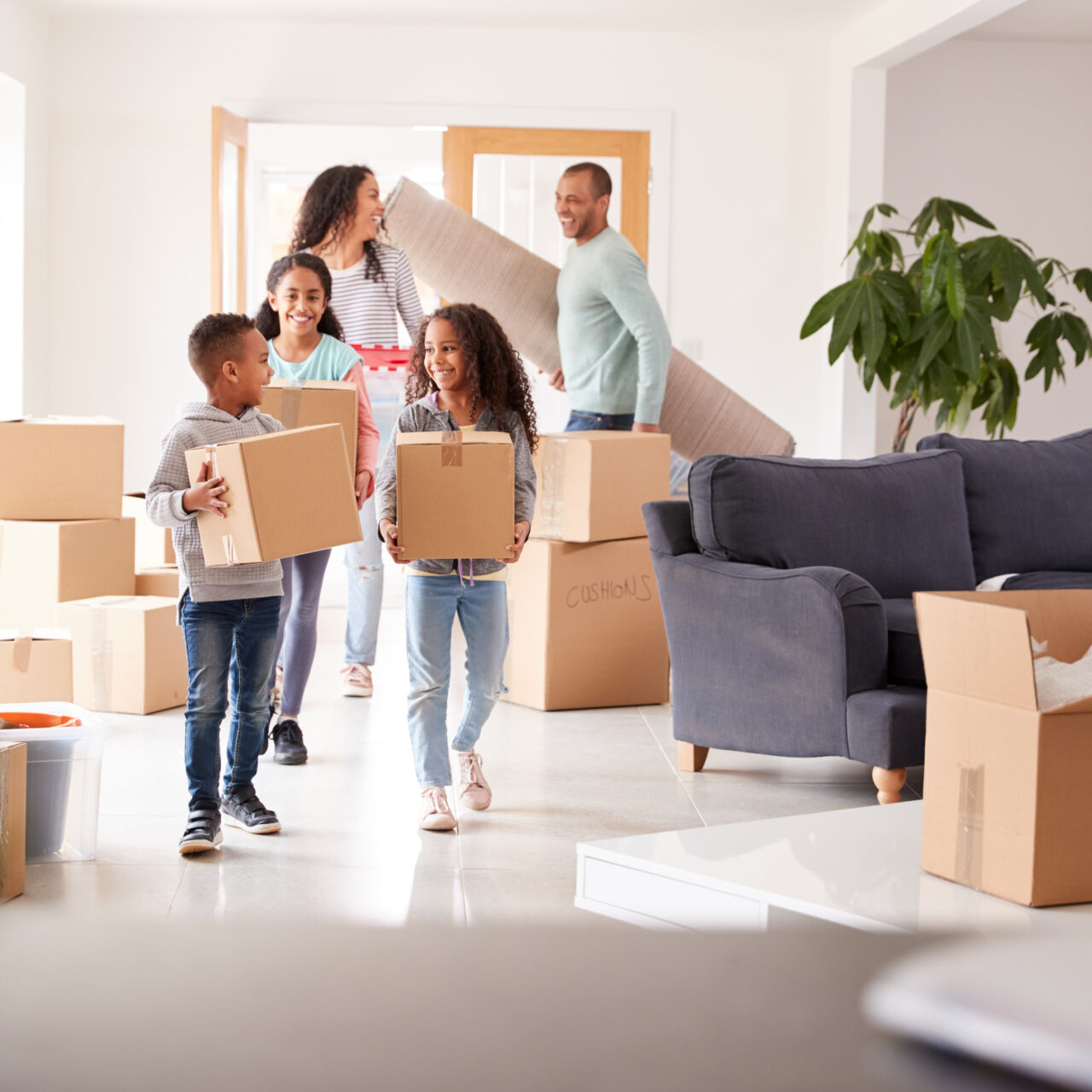 Smiling Family Carrying Boxes Into New Home On Moving Day